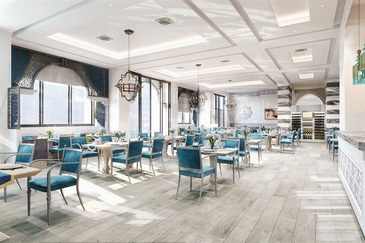 Grand Swiss-Belhotel Waterfront Seef Sanabis Exterior foto The image depicts a modern dining area with a bright and airy atmosphere. It features numerous tables and chairs arranged throughout the space. The tables are set with simple, elegant decor, and the chairs are upholstered in a vibrant blue fabric. La