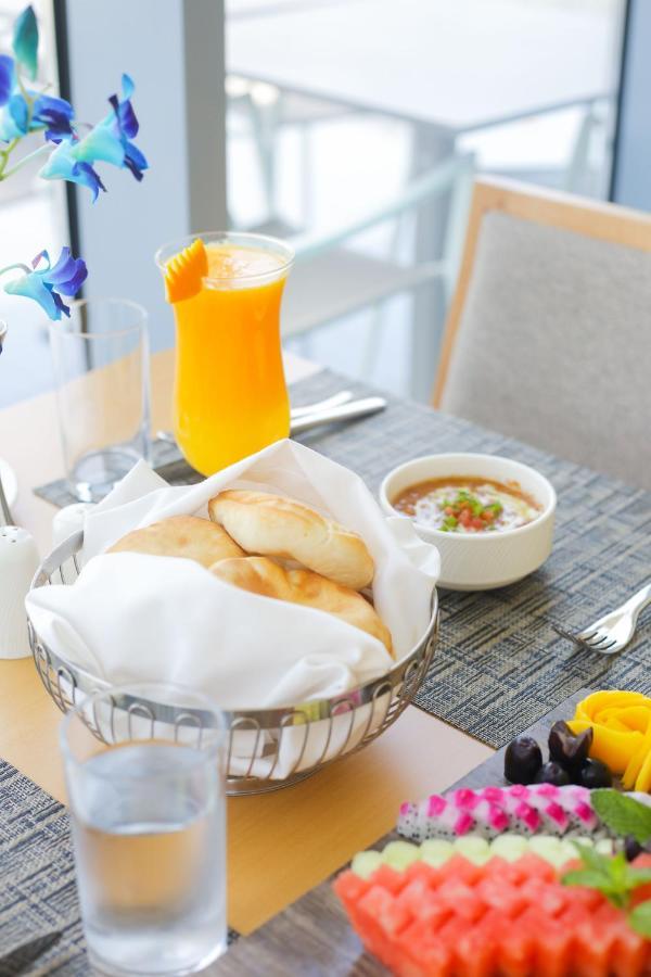 Grand Swiss-Belhotel Waterfront Seef Sanabis Exterior foto The photo shows a dining setup with a variety of food and drink. In the foreground, there is a basket lined with a white cloth containing several pieces of bread. Next to it, there’s a small bowl of a dish that appears to be a sauce or stew, garnishe