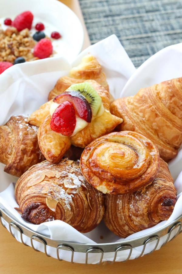 Grand Swiss-Belhotel Waterfront Seef Sanabis Exterior foto The photo showcases a variety of delicious pastries arranged on a white plate. There are croissants, possibly a fruit-filled pastry topped with sliced strawberries and kiwi, and a buttery, spiral-shaped pastry. Each item has a golden-brown color, ind